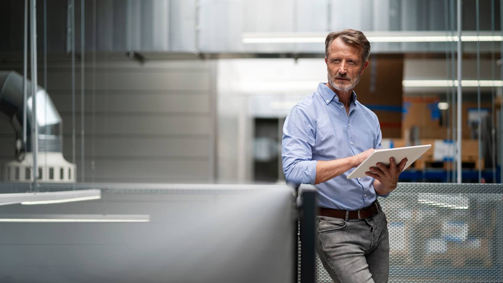 Businessman holding a tablet in his hand and leaning on a railing in a factory