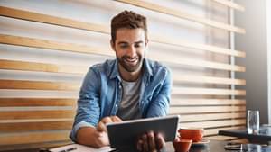 A male entrepreneur sitting and browsing in a cafe using a tablet