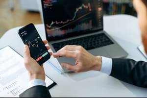 Successful male trader, investor, using a laptop and smartphone, analyzes trading charts in the stock market of a digital currency exchange, analyzes, buys and sells currencies