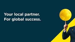 A man in a dark suit with a Commerzbank pin on his lapel balances a golden globe on his fingertip.