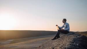 Businessman uses laptop on a rocky hill at sunset