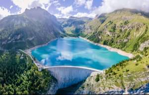 Water dam and reservoir lake in Swiss Alps mountains producing sustainable hydropower, hydroelectricity generation, renewable energy to limit global warming, aerial view, decarbonize, summer